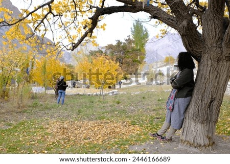 An Asian female tourist posing for a picture with the beautiful scenery of the colorful foliage at a local village in Passu Valley, Gilgit-Baltistan, Pakistan.