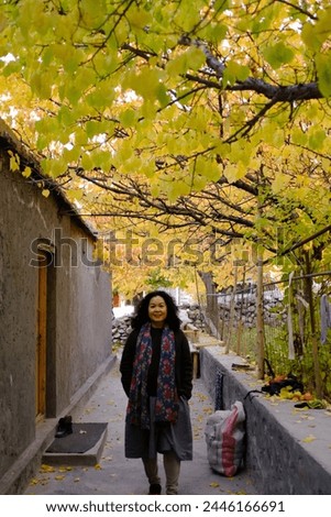 An Asian female tourist posing for a picture in a small alley with the beautiful scenery of the colorful foliage at a local village in Passu Valley, Gilgit-Baltistan, Pakistan.