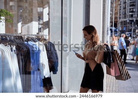 young woman taking a picture through a store window carrying shopping bags in her hand