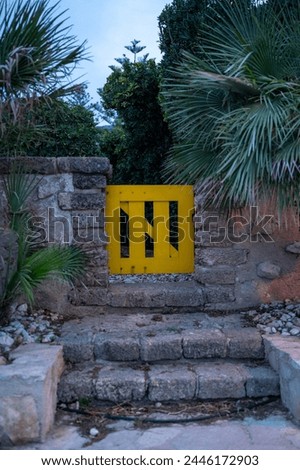 A low yellow door, entrance to a patio with palm trees and cobblestones.