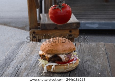 big tasty hamburger with tomato in the background
