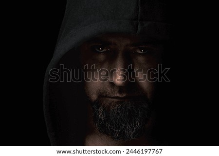 Close-up portrait of a man with a hood on a black background. Mysterious man wearing hoodies on a dark background. 