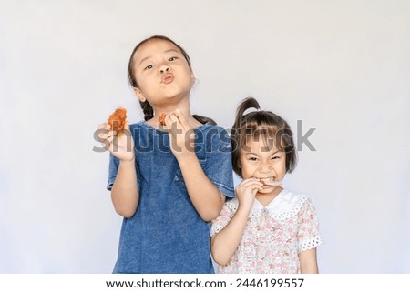 Close up portrait of two satisfied adorable Asian girls eating fried chicken. Happy small hungry kids biting fried chicken and enjoying a meal together. Children's healthy diet. Unhealthy food concept