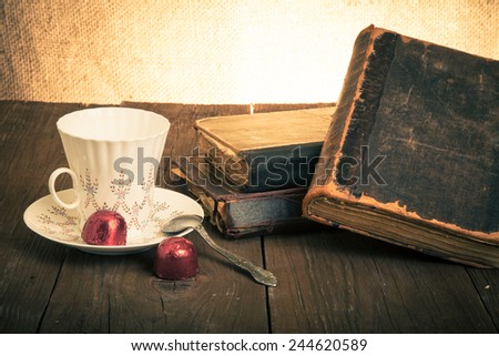 Cup of coffee, shokolad and stack of old books on the old wooden table. Toned.