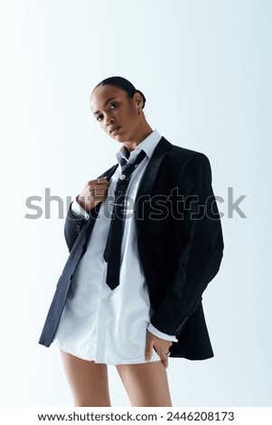 Confident young woman in her 20s, poses stylishly in a suit and tie in a studio.