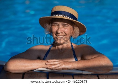 An elderly woman in a boater hat swims in the pool. Vacation in retirement.  Royalty-Free Stock Photo #2446220879