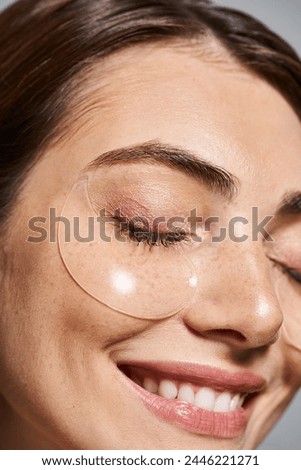 A young Caucasian woman with brunette hair applies clear under eye patches in a studio setting.