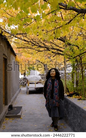 An Asian female tourist posing for a picture in a small alley with the beautiful scenery of the colorful foliage at a local village in Passu Valley, Gilgit-Baltistan, Pakistan.
