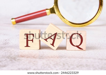 FAQ ( frequently asked questions ) text on wooden cubes on an abstract background with a magnifying glass in the background