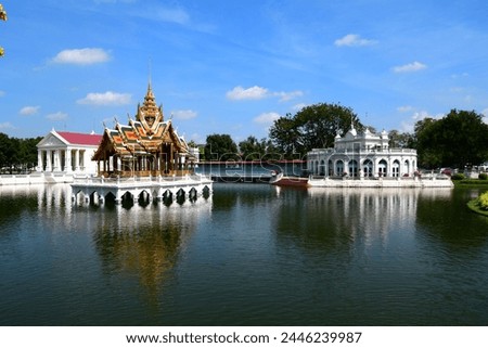 Set of three main buildings at Bang Pa In Palace in Ayutthaya, Thailand, including the Aisawan Dhiphya-Asana Pavilion , taken from the bridge. The pond in the foreground is reflected in the buildings. Royalty-Free Stock Photo #2446239987