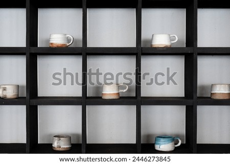 Assorted artisanal mugs display on a black shelf unit against a neutral wall showcasing minimalist design and pottery craft from handmade
