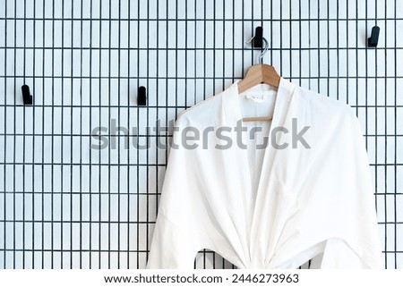 Elegant white bathrobe neatly hanging on a wooden hanger against a modern grid wall depicting clean fashion and design