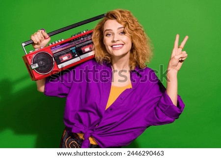 Photo portrait of pretty young hold boombox show v-sign wear trendy purple outfit isolated on green color background