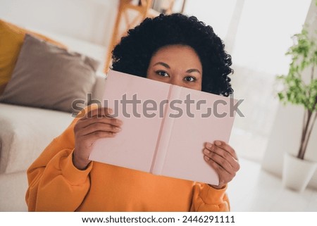 Photo portrait of lovely young lady cover face read book dressed casual orange clothes cozy day light home interior living room