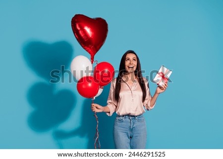 Portrait of lovely girl with long hairstyle wear silk blouse hold present box balloons look empty space isolated on blue color background