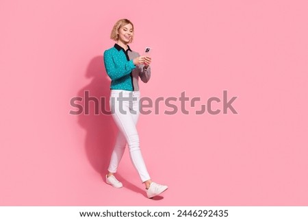 Full size photo of pretty young girl walking hold gadget wear trendy striped cyan outfit isolated on pink color background