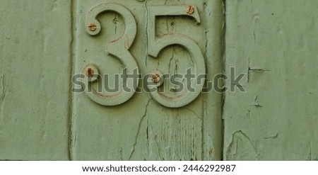 Number plate. Number thirty-five against a green wooden wall background. Concept from a room and a wall. Numbers , 3, 5. the numbers are nailed down with rusty nails. uneven textured wood surface
