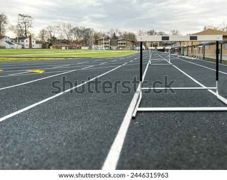 Track and Field Running Lanes. Surface level view of a line of hurdles on a running track. Hurdles are aligned to one lane on the track for practice. City neighborhood in the background of view. Royalty-Free Stock Photo #2446315963