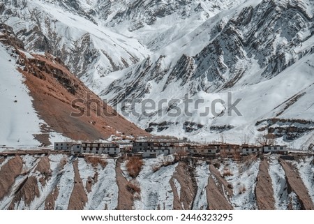 picture of a village with small population settled in a valley surrounded y snow covered mountains. Houses made from raw materials, clay, grass and wood. living in high altitude at the edge of cliff.