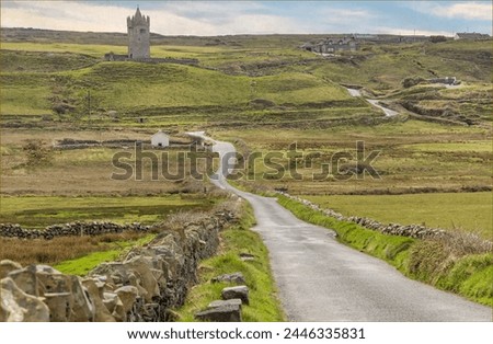 Long winding country lane leading up a hill towards to a tower Royalty-Free Stock Photo #2446335831