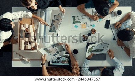 Top aerial view business people brainstorming about building interior at table with house model and laptop displayed house plan while architect engineer drawing and writing at blueprint. Alimentation. Royalty-Free Stock Photo #2446347567