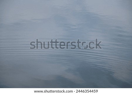Background of gentle waves forming on calm water. Clouds are reflected in the water.