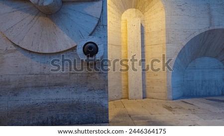 a brutalist wall with rounded arches, a round hole in the center of one arch is illuminated by an LED light bulb, snow on ground, evening blue sky, concrete texture, architectural photography 