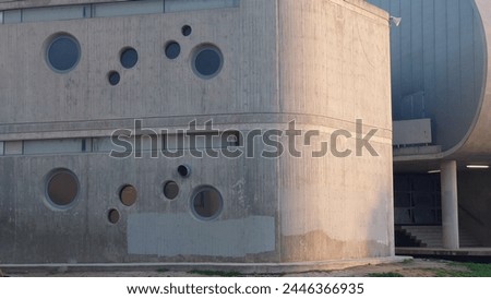 A close up photo of the curved corner and exterior walls, concrete panels, concrete frames with round windows, small birds eye view, evening light, concrete modern museum building 