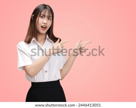 Portrait Asian student girl with Thai university uniform pointing finger isolated on pink background.