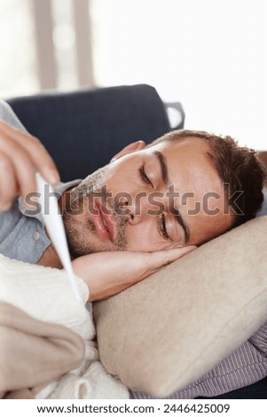 Man in living room, sick and thermometer for fever, healthcare and wellness with virus, viral infection or bacteria. Burnout, fatigue and health fail, monitor condition for illness with flu at home Royalty-Free Stock Photo #2446425009
