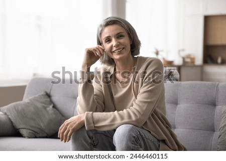 Cheerful mature woman relaxing on sofa, look at camera having appealing appearance, perfect white smile, pose for photo at home, feel happy and satisfied, looks peaceful and confident, enjoy weekend