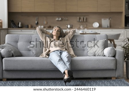Peaceful middle-aged woman sitting rest on cozy sofa in living room, leaning back with hands behind head, enjoy lazy weekend, enjoy daytime nap at modern home. Fatigue relief, take break, relaxation Royalty-Free Stock Photo #2446460119