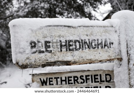 Exterior photo view of a street road sign board indicaing the direction of city town village in England UK United kigndom suring winter covered with snow ans ice freezing weather white 