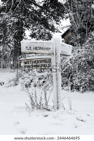 Exterior photo view of a street road sign board indicaing the direction of city town village in England UK United kigndom suring winter covered with snow ans ice freezing weather white 