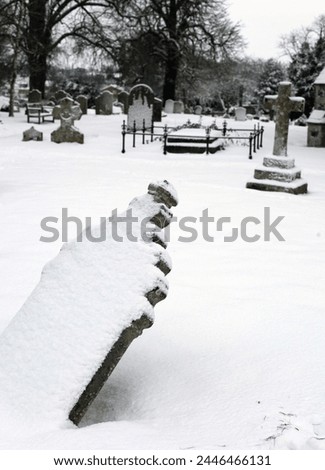 Exterior photo view of an old ancient english cemetery during winter with the snow covering all the stone crosses and tombstones during the cold front snowy icy weather