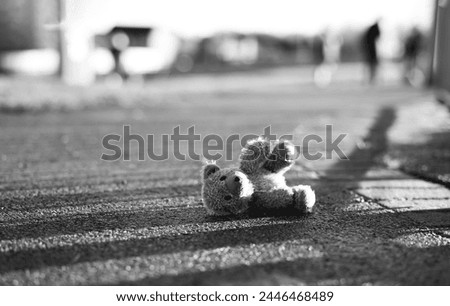 Teddy bear with sad face lying on footpath with blurry people,Image Black,White Lonely bear doll laying down on the road in gloomy day,Lost toy,Loneliness concept, International missing Children