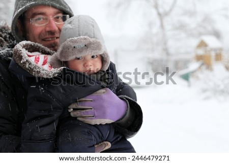 England, Europe - 12 18 2010 : Exterior photo view of a father and his baby boy child children in the snow snowy cold winter weather cold front in park garden portrait family carry 