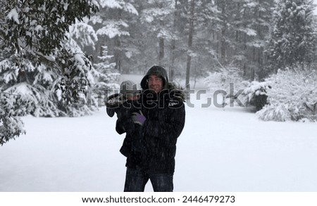 England, Europe - 12 18 2010 : Exterior photo view of a father and his baby boy child children in the snow snowy cold winter weather cold front in park garden portrait family carry 