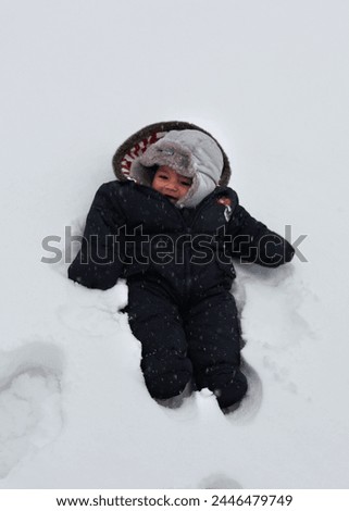 England, Europe - 12 18 2010 : Exterior photo view of a new baby born kid boy child children playing in the snow snowy cold winter weather cold front sitting alone on the white snow frozen