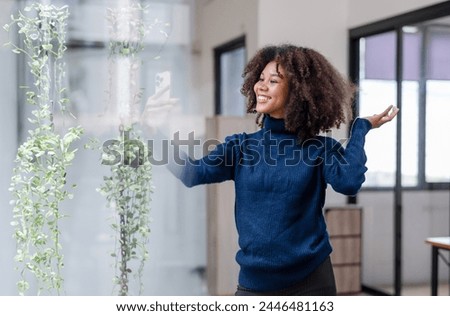 Smiling curly-haired woman enjoying taking a selfie with her smartphone in a bright and airy office space.
