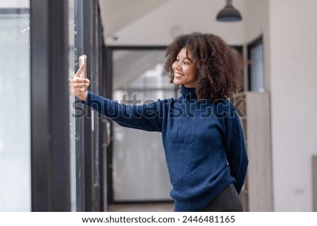 Smiling curly-haired woman enjoying taking a selfie with her smartphone in a bright and airy office space.
