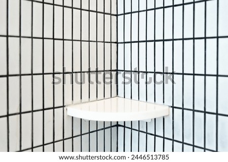 Little shelf for place shampoo, conditioner and foam stand out against a white ceramic tiles and white grid pattern on a wall capturing the essence of minimalist interior design of bathroom