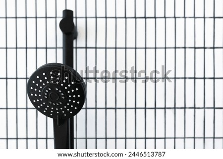 Matte black shower head is contrasting white grid pattern of ceramic tiles background showcasing contemporary bathroom design