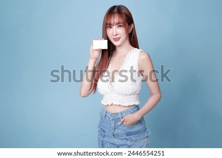 A woman is holding a white card in her hand. She is smiling and posing for the camera. The card appears to be a business card, and the woman is wearing a white shirt and blue jeans