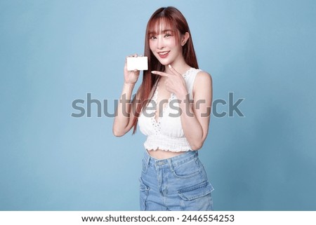 A woman is holding a white card in her hand. She is smiling and posing for the camera. The card appears to be a business card, and the woman is wearing a white shirt and blue jeans