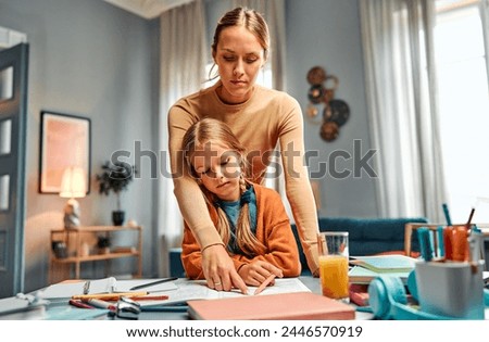 Concept of strict upbringing. Demanding mom hanging over kid from behind and pointing at mistake done in notebook. Serious child learning being attentive and responsible while doing home tasks. Royalty-Free Stock Photo #2446570919