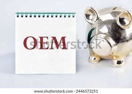 OEM original equipment manufacturer concept. Text on a white notebook on a gray background near a piggy bank in the shape of a pig