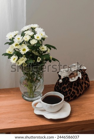 A cozy moment of the day - a cup of coffee, a bouquet of chrysanthemums in a vase, a cosmetic bag on a wooden bench in the living room