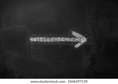 White arrow hand painted with chalk on a black blackboard indicating the direction