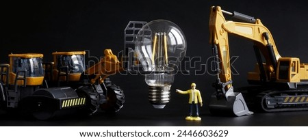 Toy tractor, construction equipment and a worker prepare to install and mount an LED bulbs. Transport, loading, unloading and installation services for fragile goods. Toy world. Photo. Close-up